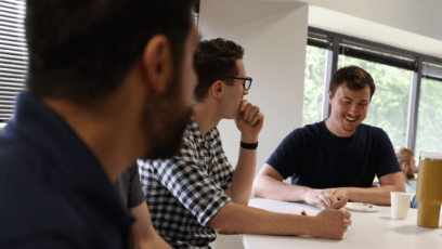 Group of people having a casual meeting around a table with discussions and laughter in a bright office environment