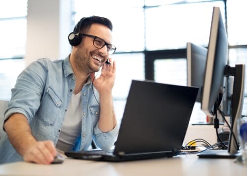 Outsourced sales development rep on video call using headset and laptop in a modern office.